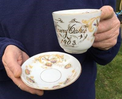 The china teacup and saucer are highly decorated with a floral pattern and dated 1903